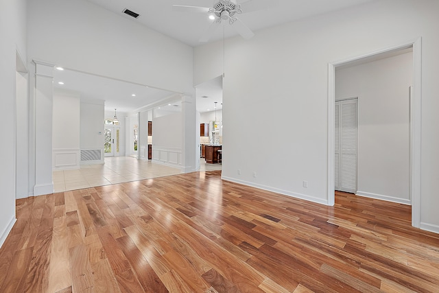 unfurnished living room with light wood-type flooring, visible vents, a decorative wall, and ceiling fan with notable chandelier