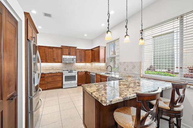 kitchen featuring visible vents, brown cabinetry, stainless steel appliances, a kitchen bar, and pendant lighting