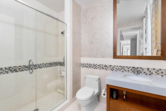 bathroom featuring a shower with shower door, tile walls, decorative backsplash, vanity, and toilet