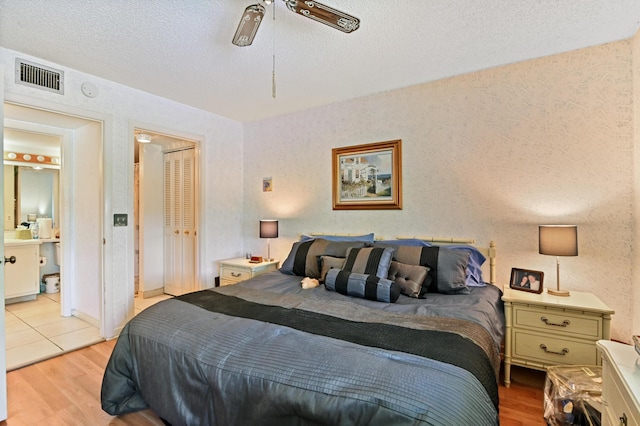 bedroom featuring ensuite bathroom, ceiling fan, a textured ceiling, light wood-type flooring, and a closet