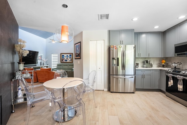 kitchen featuring pendant lighting, backsplash, vaulted ceiling, light wood-type flooring, and stainless steel appliances