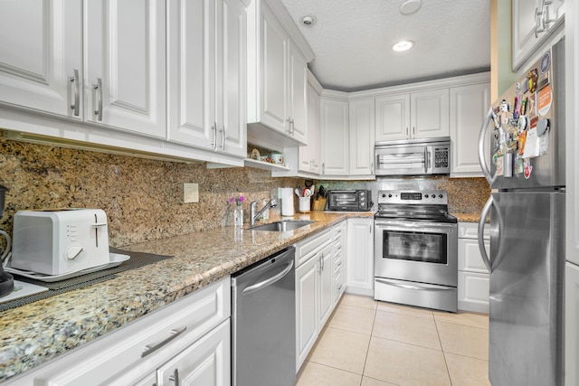 kitchen featuring light stone countertops, stainless steel appliances, sink, light tile patterned floors, and white cabinets