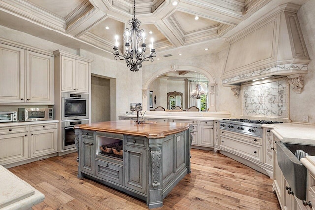 kitchen with a notable chandelier, gray cabinetry, butcher block counters, appliances with stainless steel finishes, and custom range hood