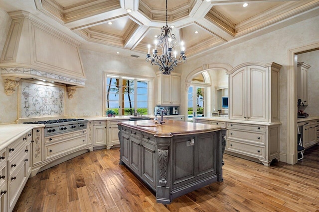 kitchen featuring cream cabinetry, a center island with sink, stainless steel gas cooktop, custom exhaust hood, and gray cabinetry