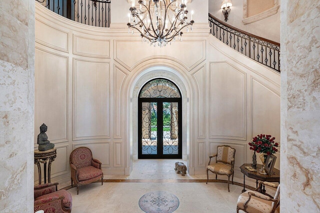 entrance foyer featuring arched walkways, a chandelier, a decorative wall, a towering ceiling, and french doors