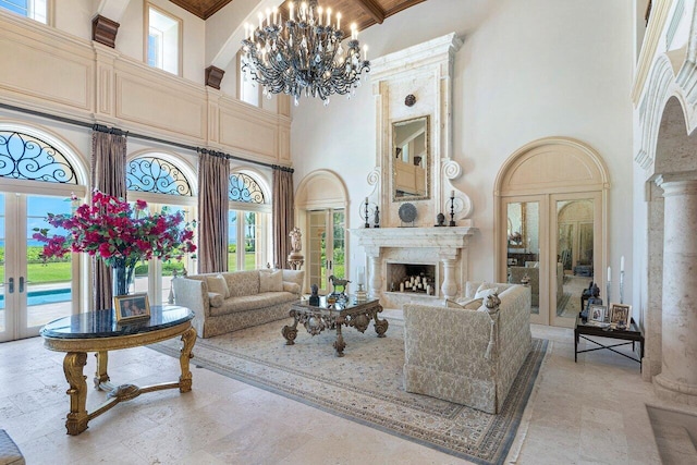 living room with a towering ceiling, french doors, a fireplace, a chandelier, and beam ceiling