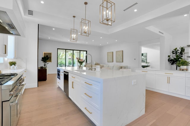 kitchen featuring wall chimney range hood, light wood-type flooring, range with two ovens, an island with sink, and sink