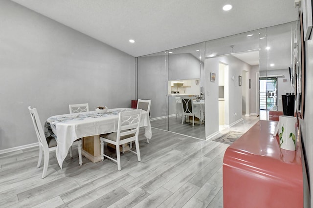 dining space with light wood-type flooring, a textured ceiling, and vaulted ceiling