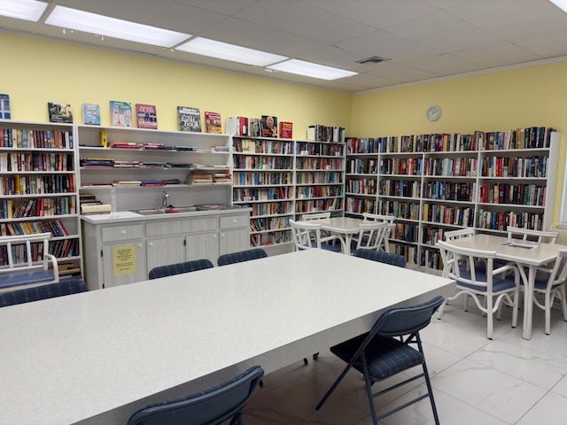 office featuring marble finish floor, a paneled ceiling, visible vents, a sink, and wall of books