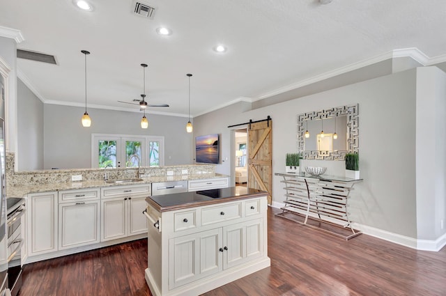 kitchen featuring dark wood-type flooring, hanging light fixtures, ceiling fan, a barn door, and white cabinetry