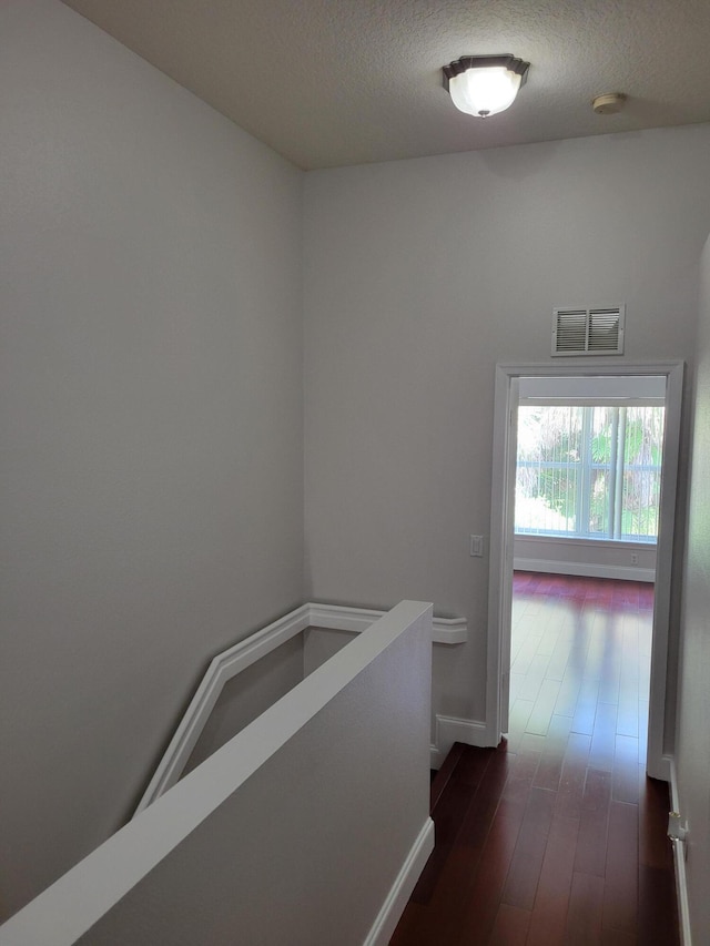 corridor with a textured ceiling and dark wood-type flooring