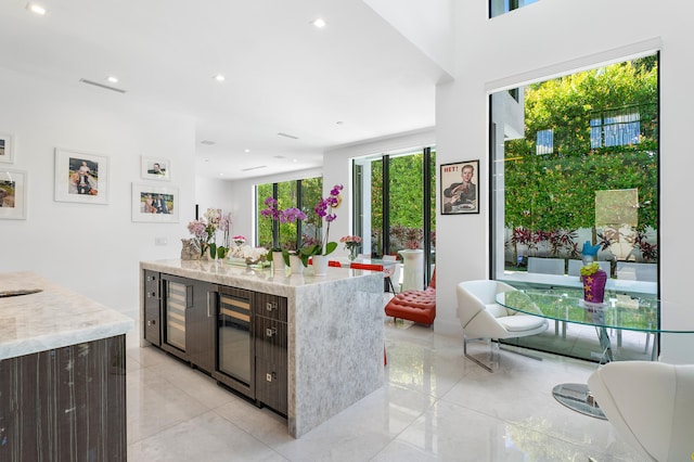 kitchen with a center island, beverage cooler, light stone counters, and light tile floors