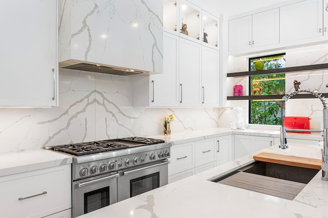 kitchen featuring light stone counters, tasteful backsplash, white cabinetry, double oven range, and premium range hood