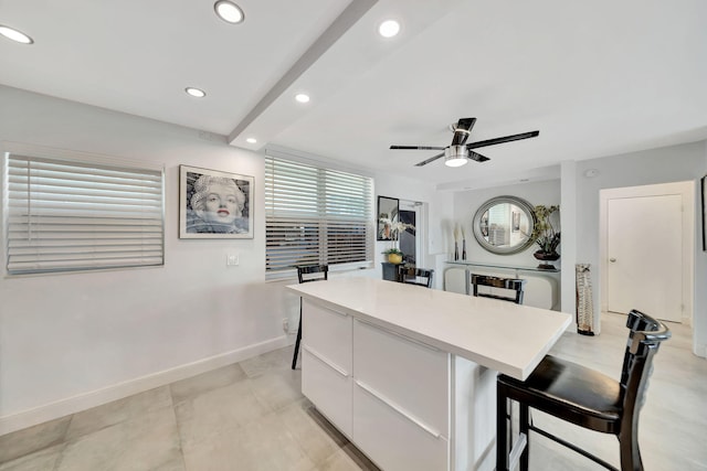 kitchen featuring white cabinets, ceiling fan, a kitchen island, and a kitchen breakfast bar