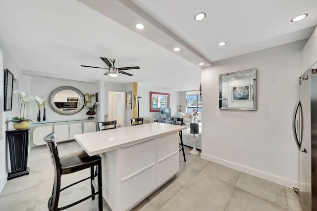 kitchen with a breakfast bar, a kitchen island, ceiling fan, white cabinets, and stainless steel refrigerator