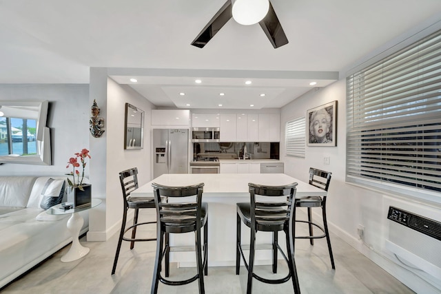 kitchen featuring decorative backsplash, a kitchen breakfast bar, stainless steel appliances, ceiling fan, and white cabinetry