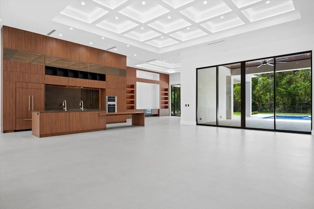 unfurnished living room featuring coffered ceiling, ceiling fan, built in shelves, a high ceiling, and sink