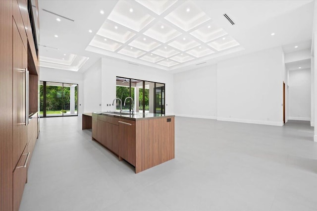 kitchen featuring a healthy amount of sunlight, coffered ceiling, a towering ceiling, and a center island with sink