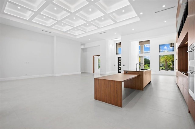 kitchen with coffered ceiling, a large island with sink, beam ceiling, a high ceiling, and sink