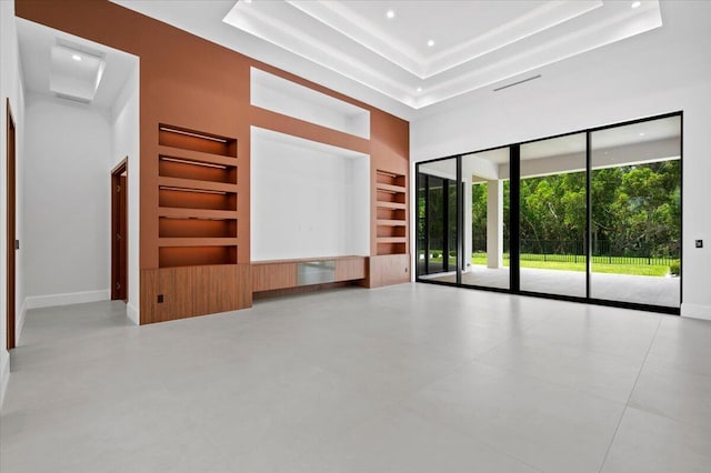 unfurnished living room featuring a high ceiling, built in features, and a tray ceiling