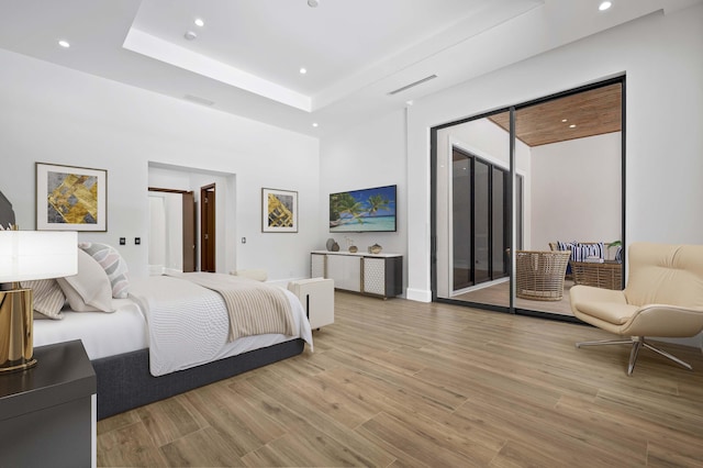 bedroom with access to outside, light wood-type flooring, and a raised ceiling