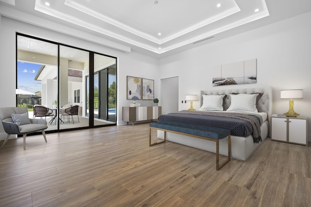 bedroom featuring access to exterior, hardwood / wood-style flooring, and a tray ceiling