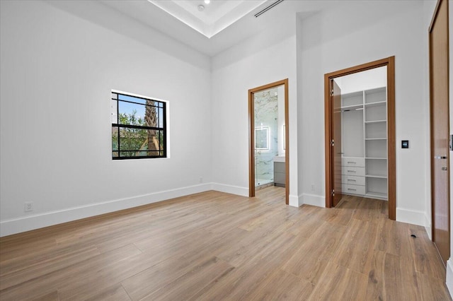 unfurnished bedroom featuring ensuite bathroom, light hardwood / wood-style floors, and a spacious closet