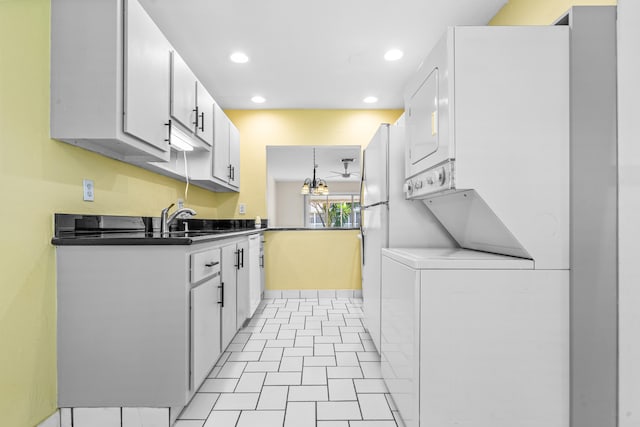 kitchen with sink, white cabinets, stacked washer / drying machine, and an inviting chandelier