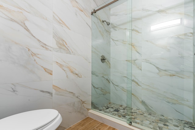 bathroom with hardwood / wood-style floors, toilet, and a tile shower