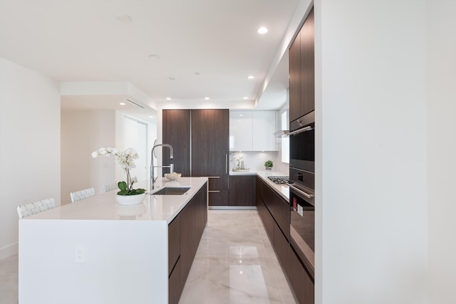 kitchen with a kitchen island with sink, sink, appliances with stainless steel finishes, white cabinetry, and dark brown cabinetry