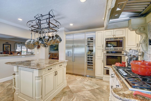 kitchen featuring a center island, light stone counters, built in appliances, crown molding, and a textured ceiling