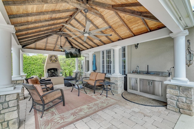 view of patio with ceiling fan, sink, an outdoor kitchen, an outdoor living space with a fireplace, and a gazebo