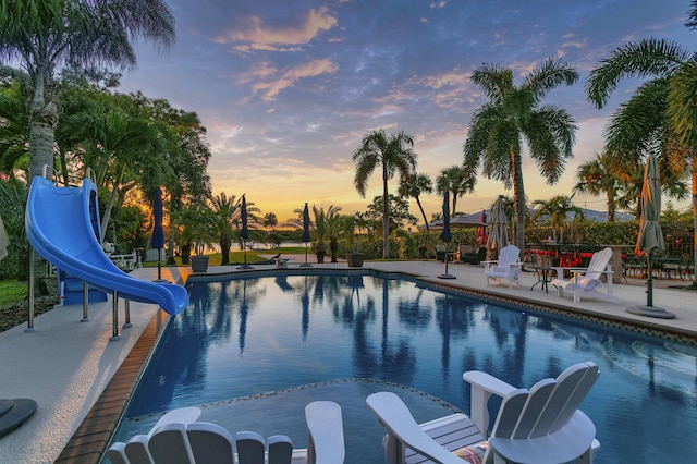 pool at dusk with a patio area and a water slide