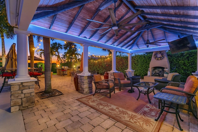 patio terrace at dusk with a gazebo, ceiling fan, and an outdoor living space with a fireplace