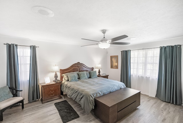 bedroom with ceiling fan, light hardwood / wood-style floors, a textured ceiling, and multiple windows