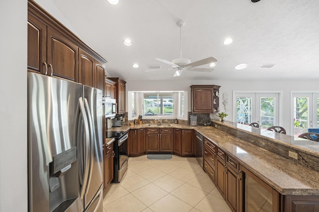 kitchen featuring ceiling fan, french doors, kitchen peninsula, dark stone counters, and appliances with stainless steel finishes