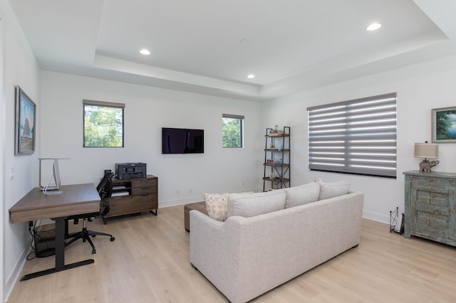 living room featuring light wood-type flooring, a tray ceiling, and a wealth of natural light