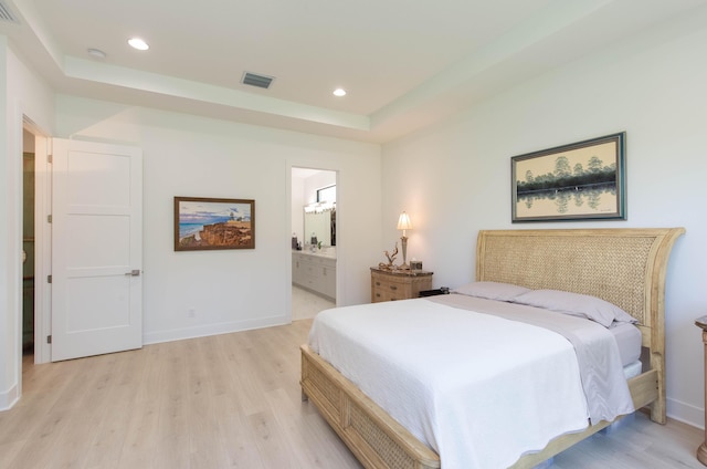 bedroom with ensuite bathroom, a tray ceiling, and light hardwood / wood-style flooring