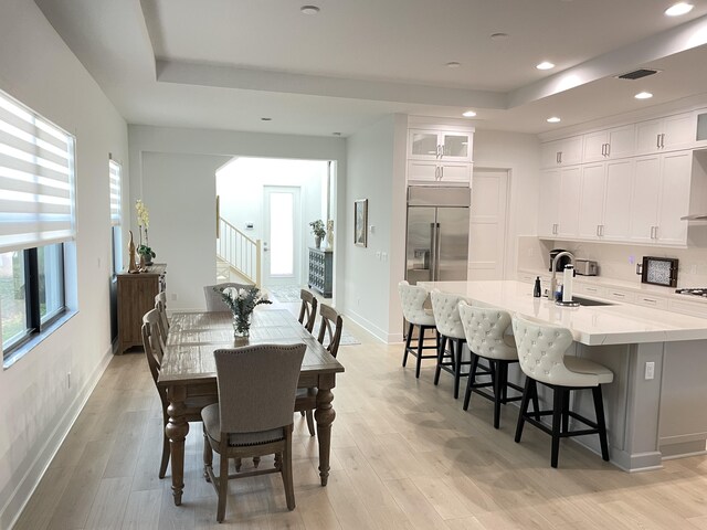 dining space with a raised ceiling, light wood-type flooring, and sink