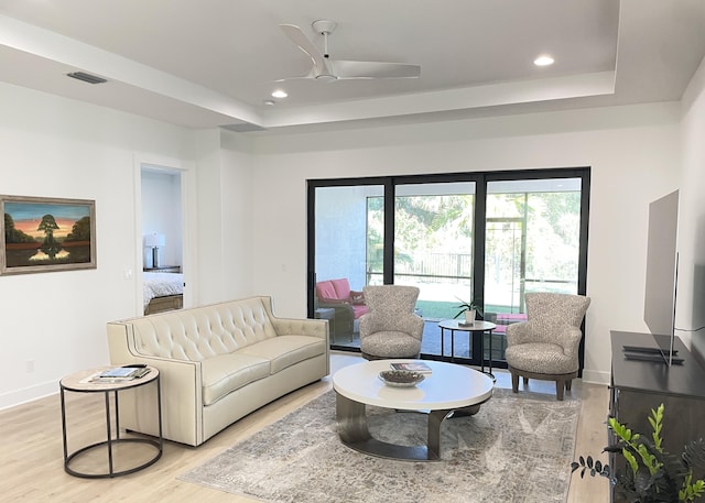 living room featuring ceiling fan, a raised ceiling, and light hardwood / wood-style flooring