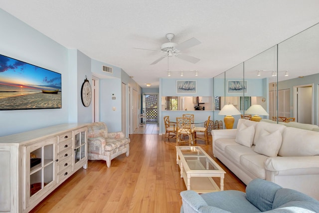 living room with ceiling fan, a textured ceiling, and light hardwood / wood-style floors