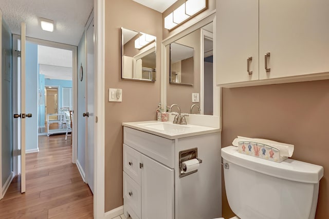 bathroom featuring vanity, wood-type flooring, a textured ceiling, and toilet