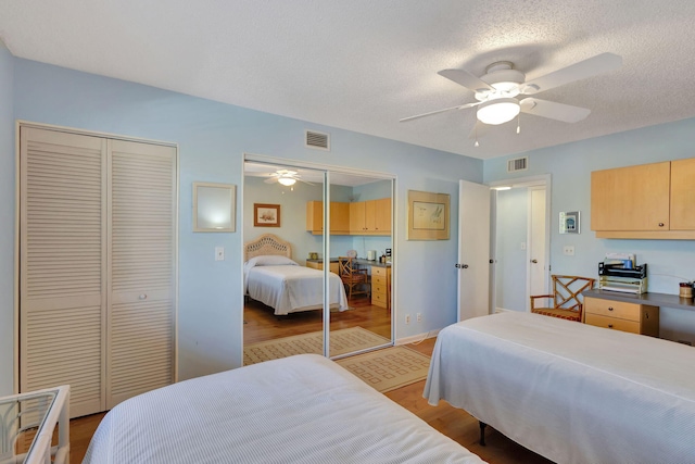 bedroom featuring ceiling fan, two closets, a textured ceiling, and light hardwood / wood-style floors