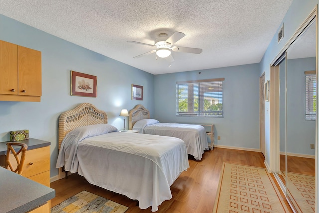 bedroom with ceiling fan, a closet, light hardwood / wood-style flooring, and a textured ceiling