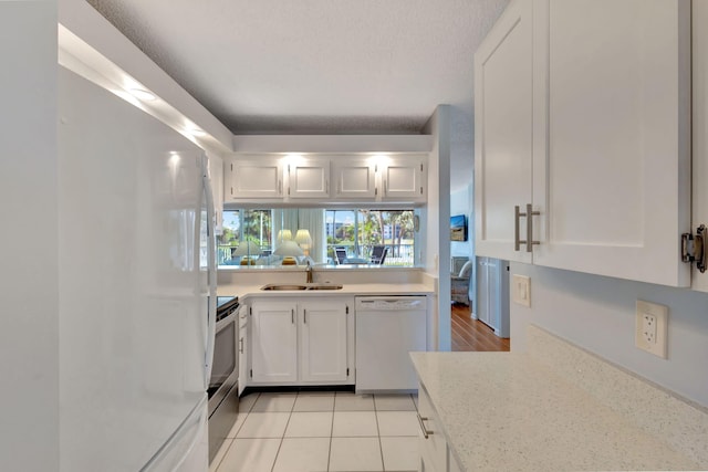 kitchen with sink, white cabinetry, light tile patterned floors, white appliances, and light stone countertops