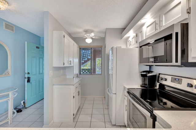 kitchen featuring appliances with stainless steel finishes, light tile patterned floors, white cabinets, and a textured ceiling