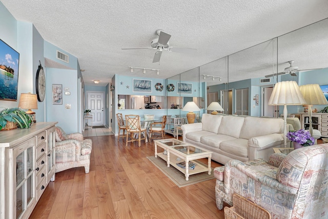 living room with light wood-type flooring, a textured ceiling, rail lighting, and ceiling fan