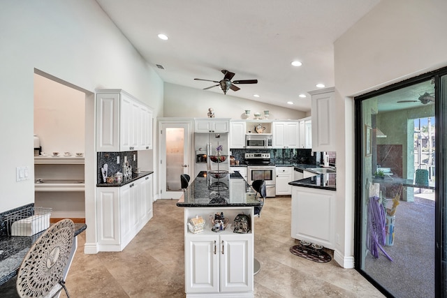 kitchen featuring tasteful backsplash, stainless steel appliances, dark stone countertops, white cabinetry, and lofted ceiling