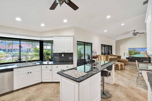 kitchen featuring stainless steel dishwasher, vaulted ceiling, sink, white cabinetry, and a kitchen island