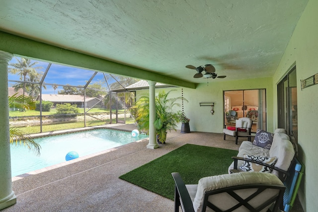 view of pool with a lawn, ceiling fan, a patio area, and glass enclosure